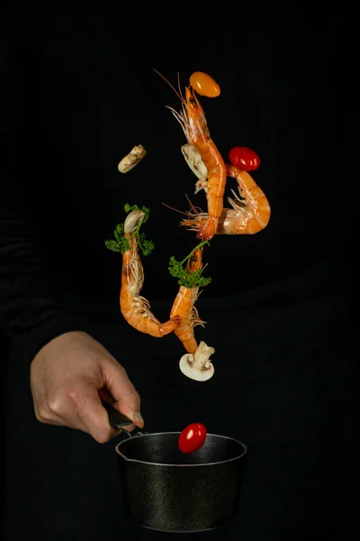 Taze iştah açıcı karides siyah bir arka planda siyah bir tavaya düşer.