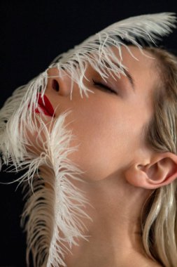 Güzel bir kız büyük beyaz bir tüyle poz veriyor.