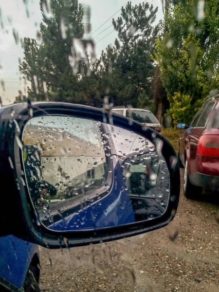 Side car mirror in the rain. Double reflection of a house with an orange roof. Drops of water on the glass.