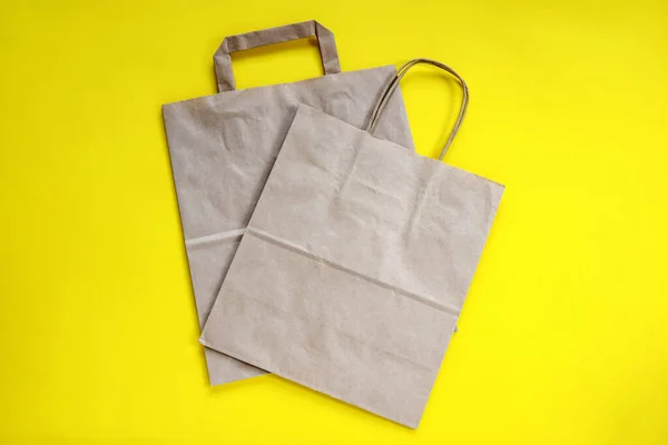 Recycled brown paper shopping bag with handle, isolated on yellow background, flat lay, mockup. Two folded empty paper bag. Close-up. Selective focus. Copy space.