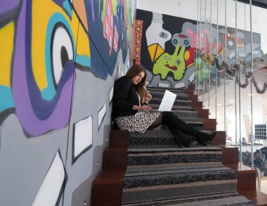 Kız ofiste merdivenlerde oturan dizüstü bilgisayar ile 