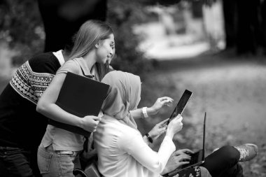 Dizüstü ve tablet bir bankta kullanarak, eğleniyor, konuşurken, dışarı asılı gençlerin grup