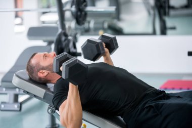Genç yakışıklı yetişkin erkek halter satırlar modern bir spor salonu bankta yapıyor