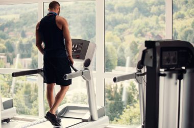 Spor giyimli genç adam spor salonunda koşu bandında koşuyor