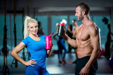 Spor, fitness, yaşam tarzı ve insanlar kavramı - erkek ve kadın spor salonunda konuşurken protein shake şişeyle gülümseyen