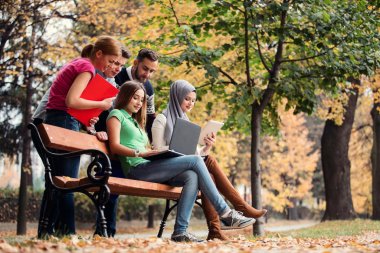 Dizüstü ve tablet bir bankta kullanarak, eğleniyor, konuşurken, dışarı asılı gençlerin grup