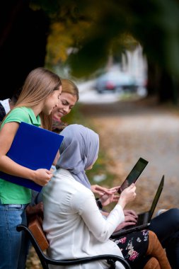 Dizüstü ve tablet bir bankta kullanarak, eğleniyor, konuşurken, dışarı asılı gençlerin grup