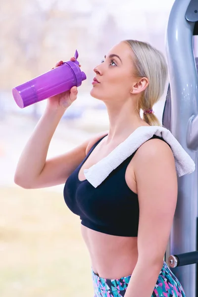 Professional bodybuilding athlete relax after exhausting training. Athlete relax and drink water from sport bottle in gym interior.