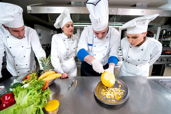 Kitchen chef with young apprentices, teaching to make decorative fruit basket