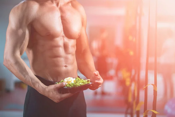 bodybuilder eating salad in the gym