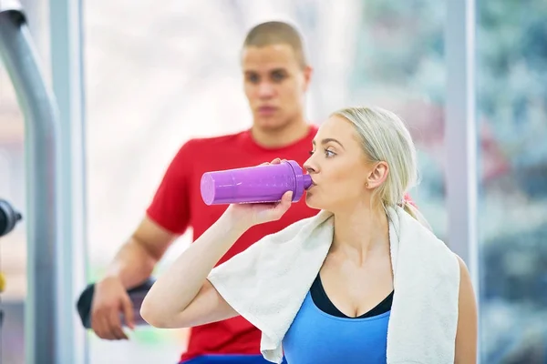 Professional bodybuilding athlete relax after exhausting training. Athlete relax and drink water from sport bottle in gym interior.