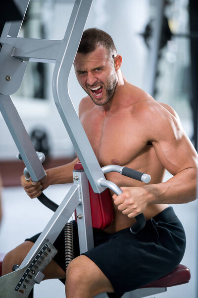 Determined young muscular man working on fitness machine at the gym