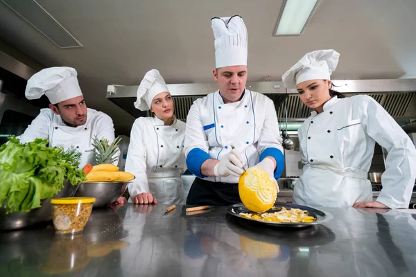 Kitchen chef with young apprentices, teaching to make decorative fruit basket
