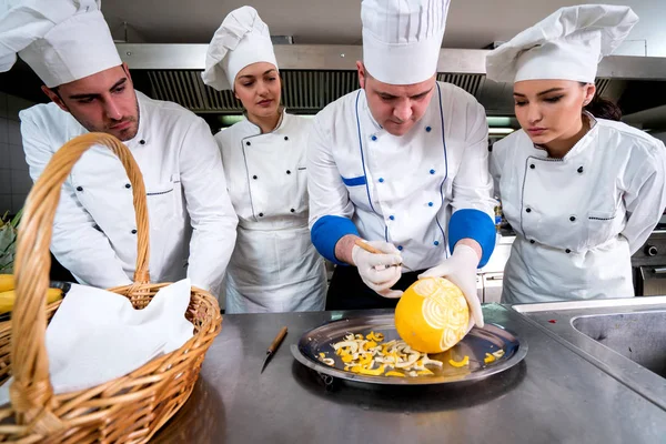 Kitchen chef with young apprentices, teaching to make decorative fruit basket