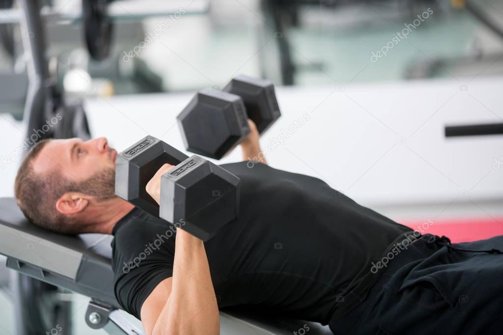 Young handsome adult male doing dumbbell rows on bench in modern gym