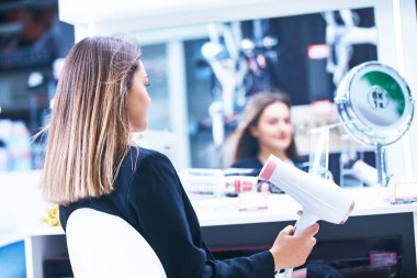 Saç bakım. Güzel uzun saçlı kadın elektronik mağazasında saç kurutma
