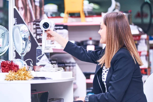 Saç bakım. Güzel uzun saçlı kadın elektronik mağazasında saç kurutma