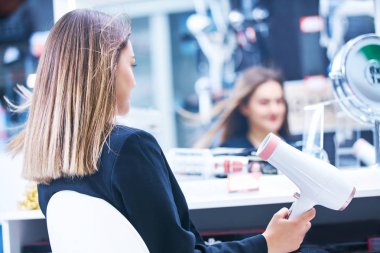 Saç bakım. Güzel uzun saçlı kadın elektronik mağazasında saç kurutma