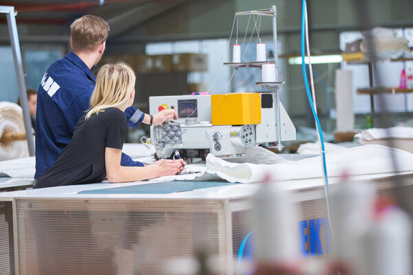 Seamstress is new assigned to a machine in a textile factory, the foreman explains something