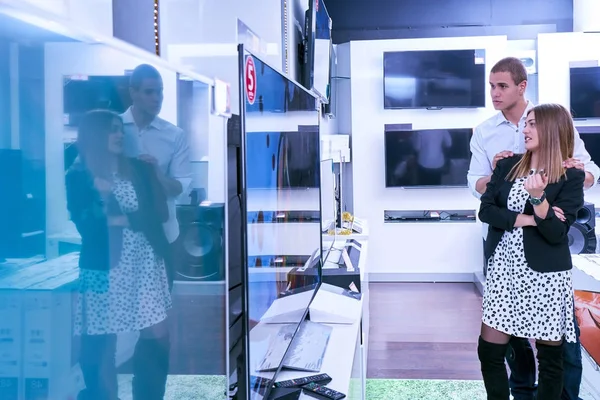 Young couple in consumer electronics store looking at latest laptop, television and photo camera to buy