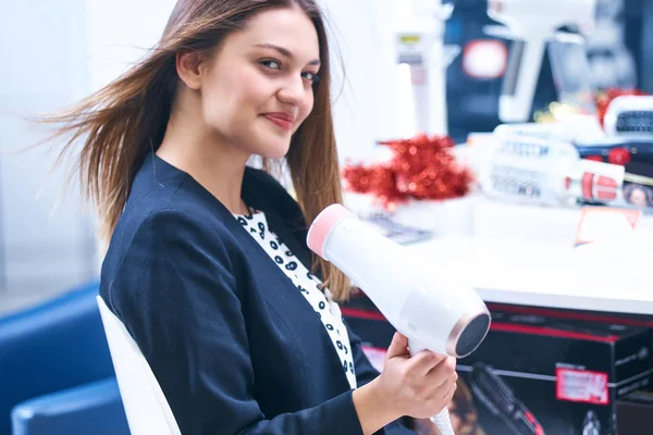 Saç bakım. Güzel uzun saçlı kadın elektronik mağazasında saç kurutma