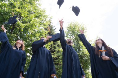Eğitim, mezuniyet ve halk konsepti. Havan topu ve diplomalı bekarlık elbisesi giyen bir grup mutlu uluslararası öğrenci.