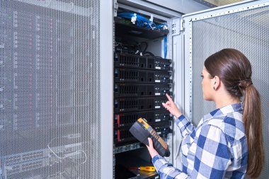 Beyaz sunucu odası açık server raf yanındaki tamirhanede sunucu üzerinde çalışan kadın teknisyeni