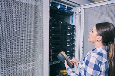 Beyaz sunucu odası açık server raf yanındaki tamirhanede sunucu üzerinde çalışan kadın teknisyeni