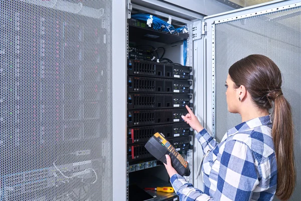 female technician working on server maintenance in white server room next to open server rack