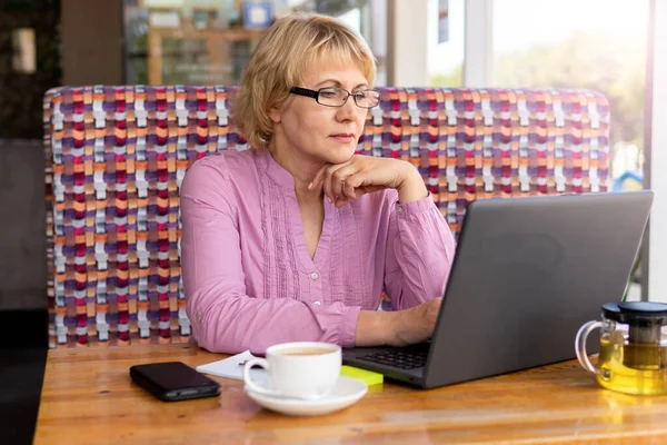 Женщина, сидящая за столом с чашкой чая и ноутбуком, работающим в кафе . — стоковое фото