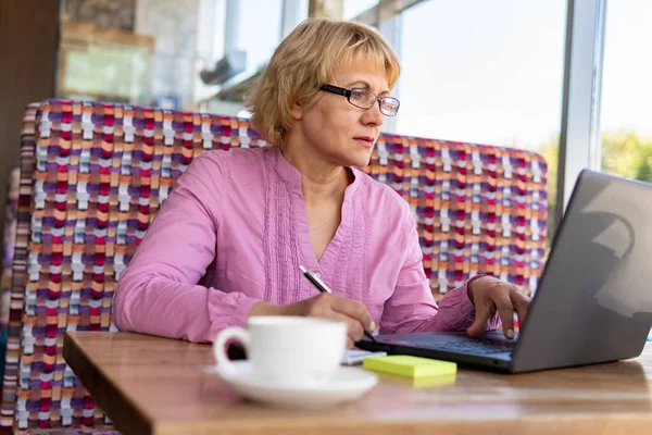 Bir fincan çay ve bir laptopla masada oturan bir kadın kafede çalışıyor..