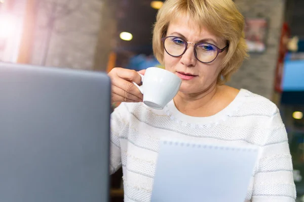 Una mujer con un portátil trabaja en un café en la oficina, es freelancer . — Foto de Stock