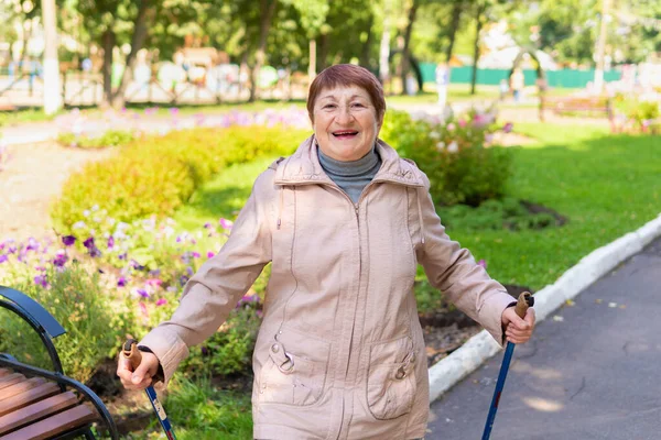 An elderly woman walks nordic with sticks in the Park on a Sunny