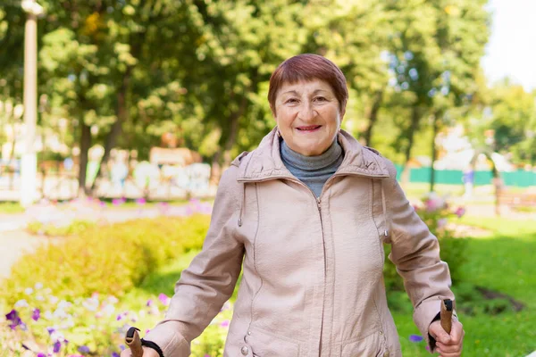 An elderly woman walks nordic with sticks in the Park on a Sunny