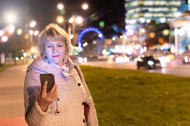 Elinde cep telefonu olan bir kadın gece şehrinde yürüyor..