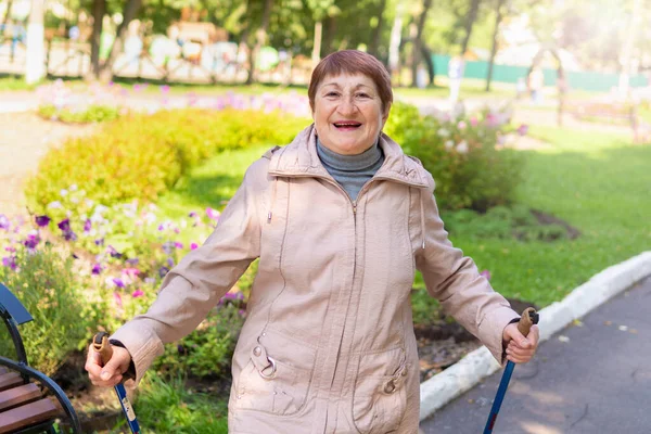 Old woman walks nordic with sticks in the Park on a Sunny summer