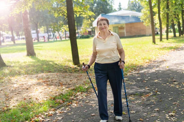 Old woman walks nordic with sticks in the Park on a Sunny summer day outdoors