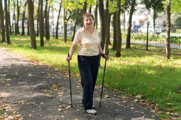 An elderly woman walks nordic with sticks in the Park on a Sunny summer day outdoors
