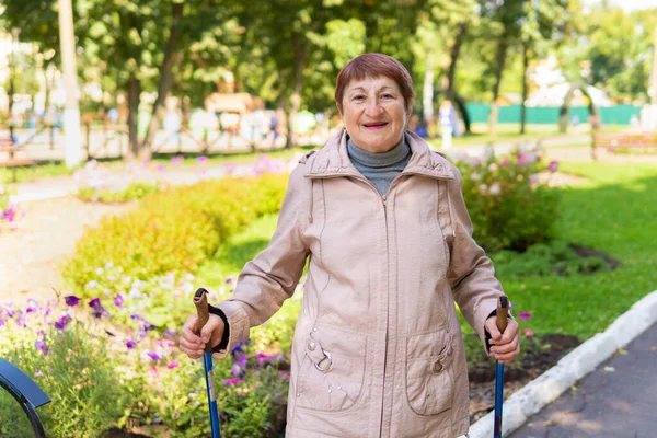 Old woman walks nordic with sticks in the Park on a Sunny summer