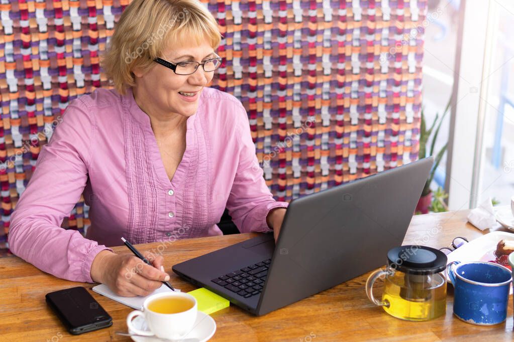 A woman sitting at a table with a Cup of tea and a laptop workin