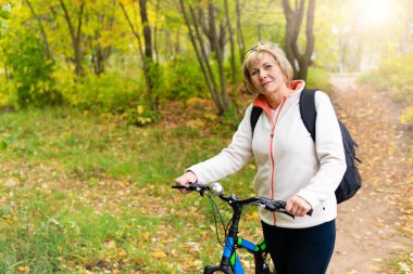 Bisiklete binen bir kadın parktaki yolda bisiklet sürüyor.