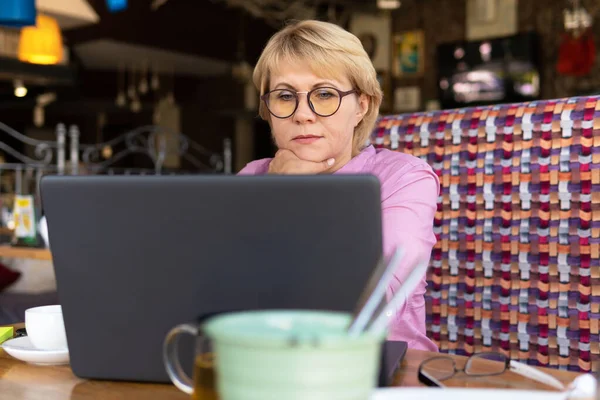Una mujer con un portátil mira un documento en un café, oficina — Foto de Stock