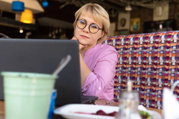 Una mujer con un portátil mira un documento en un café, oficina — Foto de Stock