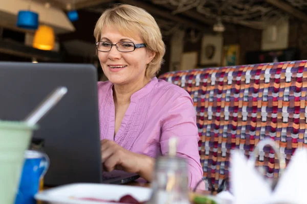 A woman with a laptop looks at a document in a cafe, office