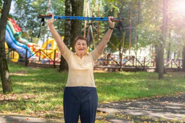 Yaşlı kadın güneşli bir yaz gününde parkta sopayla kuzeye doğru yürür.
