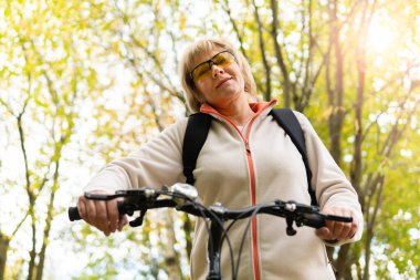 Bisiklete binen bir kadın parktaki yolda bisiklet sürüyor.