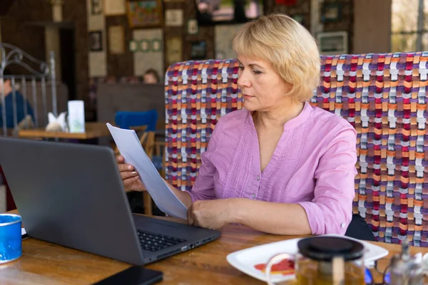 Женщина с ноутбуком смотрит на документ в кафе, офисе — стоковое фото