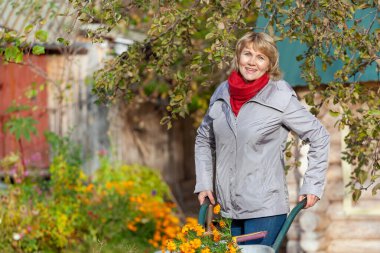 Bahçedeki kadın sebze hasat ediyor, evin arka planında meyveler ve ağaçlar..