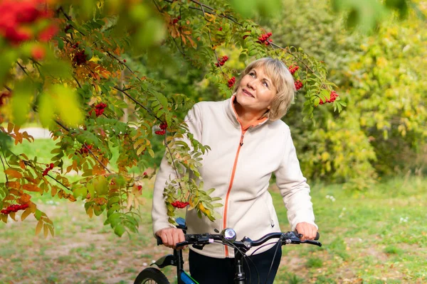 Bisikletli bir kadın sonbahar parkında ağaçların arasında bisiklet sürüyor..