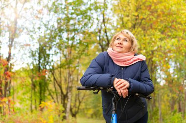 Bisikletli bir kadın sonbahar parkında ağaçların arasında bisiklet sürüyor..